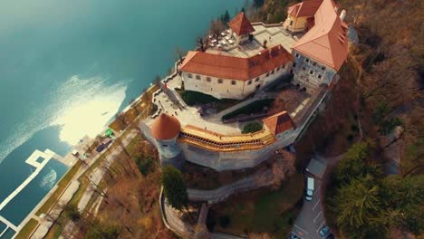 Drone-Lento-Giratorio-Hacia-La-Izquierda-Vista-Voladora-Del-Lago-Bled-Castillo-Iluminado-Por-El-Sol-En-El-Acantilado