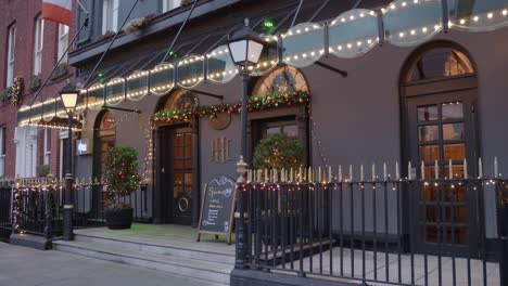 Foto-De-Lugareños-Pasando-Por-La-Entrada-Del-Hotel-Harcourt-Bellamente-Iluminado-Con-Adornos-Navideños-En-Dublín,-Irlanda.