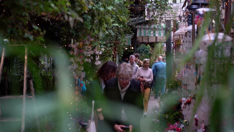 Turistas-Caminando-Por-El-Marché-Aux-Fleurs-Reina-Isabel-II-Vendiendo-Adornos-Para-Colgar,-Ambiente-Floral-Que-Rodea