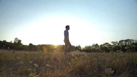 Man-walking-a-grassfield-during-sunset