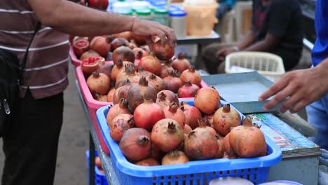 Mano-De-Mujer-Eligiendo-La-Mejor-Granada-En-Las-Tiendas-Locales,-Mercado-De-Fruta-Fresca-En-La-India,-Primer-Plano-De-Granada