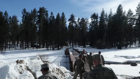 Military-men-walking-on-a-bridge-after-a-heavy-snowfall-in-the-mountains,-hand-held-shot