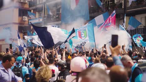 Zeitlupenaufnahme-Von-Springenden-Fußballfans,-Die-An-Einem-Sonnigen-Tag-Draußen-Auf-Der-Straße-In-Der-Stadt-Die-Meisterschaft-Von-Neapel-Feiern-–-Schwenkende-Fahnen-Und-Dekorierter-Balkon-Des-Hauses-Im-Hintergrund