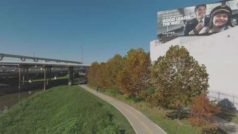 Eine-Luftaufnahme-Von-Radfahrern,-Die-Unter-Blauem-Himmel-Und-Herbstfarben-In-Houston,-Texas,-Den-White-Oak-Bayou-Trail-Hinunterfahren