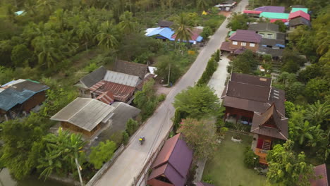 Motorradfahrer-Auf-Thailändischen-Landstraßenantennen,-Tropischer-Vegetation-Und-Authentischen-Häusern