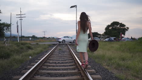 Model-Im-Sommerkleid-Balanciert-Spielerisch-Auf-Der-Bahnschiene-–-Kamerafahrt-Von-Hinten