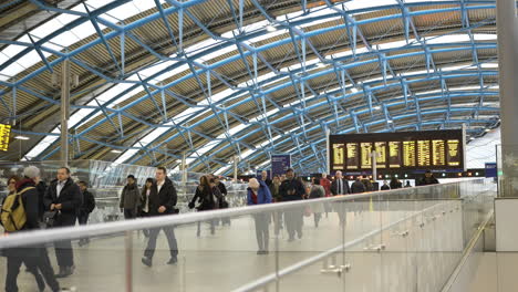 Still-shot-crowd-of-people-walking-through-train-station-with-departure-arrival-board-in-background