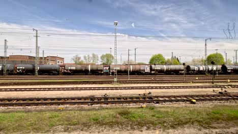 Blick-Aus-Dem-Fenster-Eines-Fahrenden-Zuges,-Der-Mit-öffentlichen-Verkehrsmitteln-Durch-Den-Güterbahnhof-In-Deutschland-Fährt-Und-An-Güterzügen-Vorbeifährt