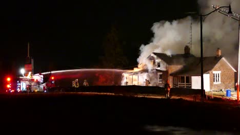 Mehrere-Feuerwehrleute-Bekämpfen-Nachts-Einen-Großen-Hausbrand,-Bei-Dem-Rauch-Aus-Dem-Gebäude-Aufsteigt