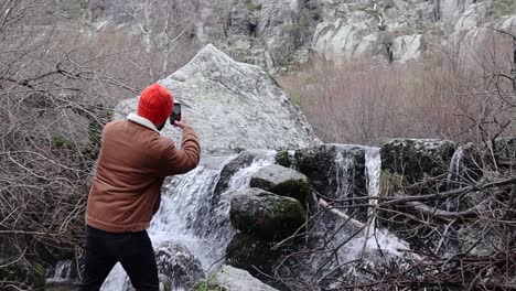 Mann,-Der-Im-Winter-Mit-Einem-Smartphone-Ein-Foto-Von-Einem-Felsigen-Bach-Macht