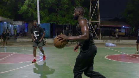 Cámara-Lenta-Siguiendo-A-Un-Jugador-Negro-De-Baloncesto-Realizando-Una-Acción-Ofensiva-De-Ataque-Durante-El-Entrenamiento-En-Una-Cancha-Al-Aire-Libre-Por-La-Noche