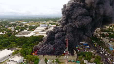 Aerial-view-of-firemen-fighting-a-structure-fire,-dark-smoke-rising-from-a-warehouse-ruins,-cloudy-day,-in-Port-au-Prince,-Haiti---tracking,-drone-shot