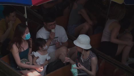 Down-Shot,-Tourist-eats-some-snacks-in-the-wooden-boat-on-Floating-Market-In-Thailand,-colorful-umbrella-in-the-background