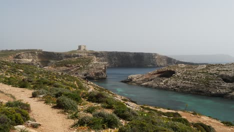 Panoramic-View-Of-Blue-And-Crystal-Laggon-With-People-Hiking,-Saint-Mary's-Tower-In-Background