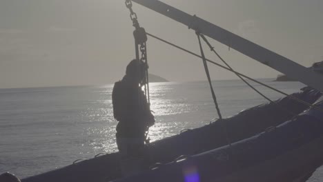 A-man-is-standing-on-a-boat-while-it-is-being-descended-from-the-cruise-ship-near-an-island-of-the-Galapagos-islands