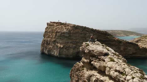 People-Standing-On-The-Cliffs,-Man-In-Foreground-Operating-A-Drone