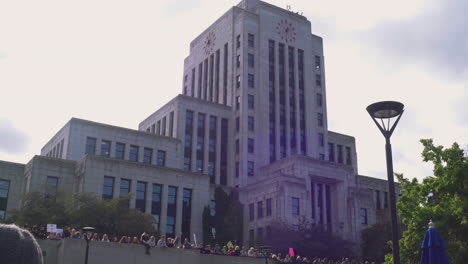 AN-UPWARD-TILT-with-Subtle-Flare-of-Vancouver-City-Hall,-Protestors-Congregate-on-its-Grounds