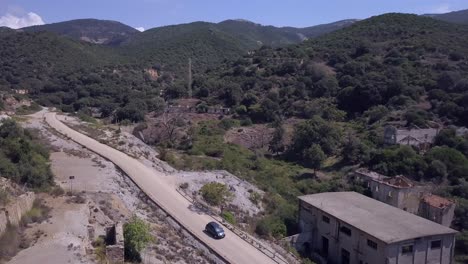 Drohnenschüsse-Fliegen-über-Die-Verlassene-Kohlenwäsche-Brassey-Auf-Sardinien,-Während-Ein-Auto-Auf-Einer-Nahegelegenen-Straße-Fährt