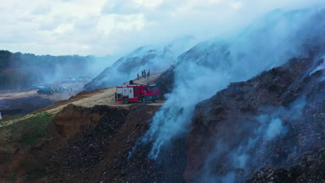 Aerial-view-over-firemen-and-firetrucks,-extinguishing-a-fire-at-a-junkyard,-in-Dominican-Republic---rising,-drone-shot