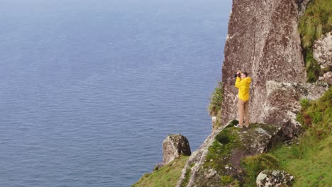 Hombre-De-Chaqueta-Amarilla-Con-Cámara-Hace-Fotos-En-Azores-Portugal,-Aérea