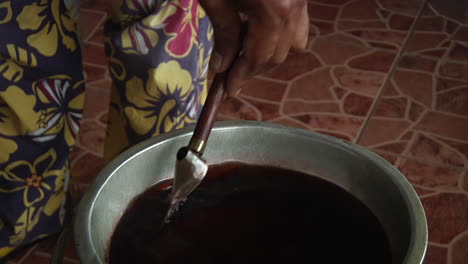 Close-View-Of-Adult-Hand-Using-Batik-Tjanting-Tool-Stirring-Hot-Wax-In-Bowl