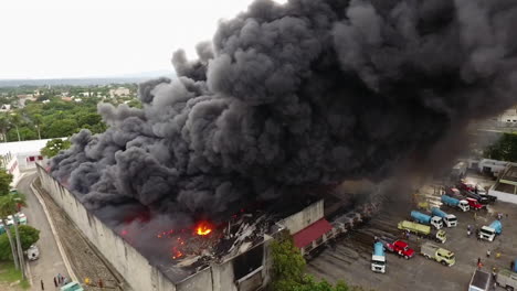 Aéreo,-Panorámico,-Drone-Disparado-Alrededor-De-Camiones-De-Bomberos-Y-Bomberos-Extinguiendo-Un-Almacén-En-Llamas,-Durante-El-Día,-En-República-Dominicana