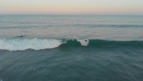 Professionelle-Surfer-Werden-Zur-Goldenen-Stunde-Von-Milden-Wellen-Am-Strand-Von-Santinho-Mitgerissen