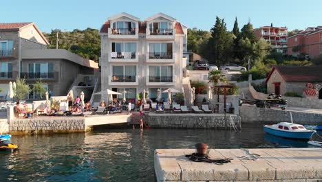 Aerial-Dolly-Reveal-of-Girl-Sunbathing-and-Children-Playing-in-Kotor-Bay,-Montenegro