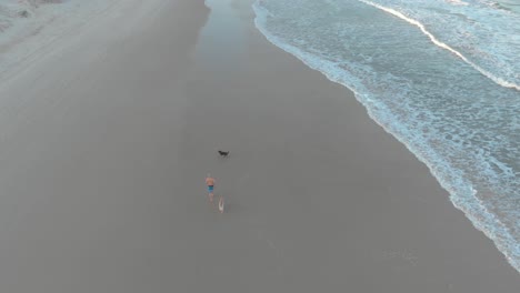 Urlaub-Am-Sandstrand-Von-Santinho-Mit-Einer-Person,-Die-Mit-Hunden-Am-Ufer-Entlangläuft