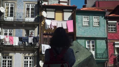 Dolly-Out-Shot,-Frau-Mit-Rotem-Rucksack,-Die-An-Einem-Sonnigen-Tag-Auf-Dem-Riberia-Platz-In-Porto-Auf-Ihrem-Balkon-Steht