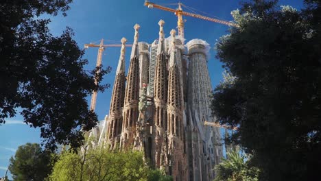 LKW-Aufnahme,-Strahlend-Blauer-Himmel,-Im-Hintergrund-Bäume,-Die-Den-Laufenden-Bau-Der-Kirche-Sagrada-Familia-Zeigen