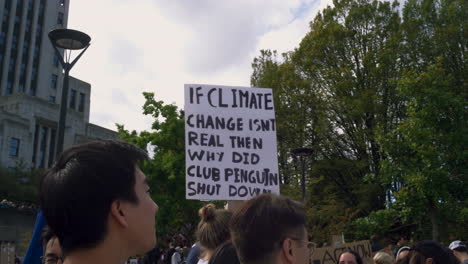 A-Climate-Change-Protester-Holding-a-Sign-with-a-Clever-Slogan,-Vancouver-City-Hall-in-the-background