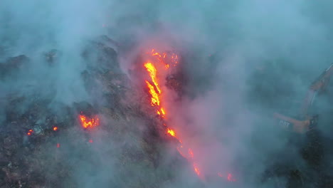 Vista-Aérea-De-Los-Bomberos-Usando-Una-Excavadora-Para-Combatir-Un-Incendio-Forestal-En-Llamas,-Humo-Oscuro-Elevándose,-Tarde-Sombría,-En-Nueva-Gales-Del-Sur,-Australia:-Disparo-De-Drones-Estáticos