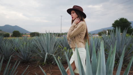 Mujer-Joven-Segura-De-Sí-Misma-Con-Sombrero-De-Vaquero-Y-Vestido-De-Verano-Cruzando-Campos-De-Piña-De-Tequila-En-México---Toma-En-Cámara-Lenta-De-Seguimiento-Medio