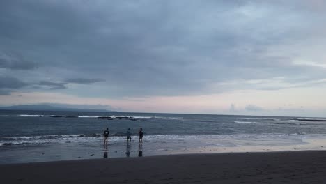 Freunde-Angeln-Allein-Am-Stürmischen-Schwarzen-Sandstrand-Von-Bali,-Indonesien,-Dunkelblaue-Silberne-Skyline,-Saba,-Gianyar