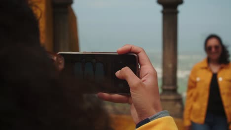 Schwenkfokusaufnahme,-Frau-Macht-Mit-Einem-Mobiltelefon-Ein-Foto-Von-Ihrer-Schwester,-Frauen-Stehen-Verschwommen-Im-Hintergrund