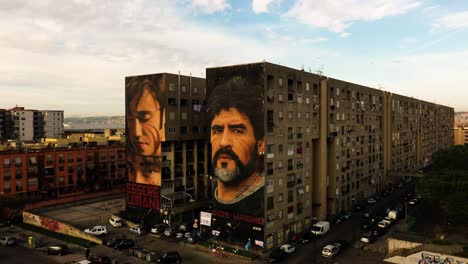 Toma-Aérea-En-órbita-Que-Muestra-La-Pintura-De-Esseri-Umani-Y-Diego-Maradona-En-La-Pared-De-Un-Bloque-De-Apartamentos-Iluminado-Por-El-Sol-Durante-La-Puesta-De-Sol---Ciudad-De-Nápoles,-Italia