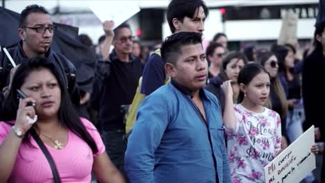 Women-and-men,-mostly-wearing-black-clothes-and-holding-signs-and-flags,-are-marching-during-a-protest-for-the-recent-killing-of-a-woman-in-the-hands-of-a-man