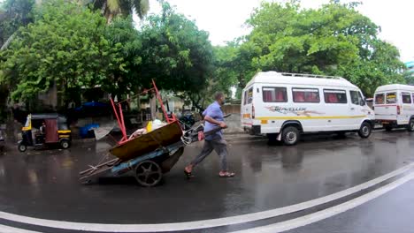 Trabajador-Masculino-Con-Mascarilla-Tirando-De-Un-Carro-Lleno-De-Cosas-En-La-Calle-En-Mumbai,-India-Bajo-La-Lluvia---Vista-De-Ojo-De-Pez---Cámara-Lenta