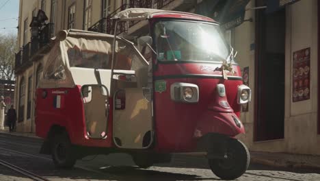 Close-up-Slow-motion-shot,-Women-driving-a-Red-Electric-Cart-turning-around-the-street-of-Lisbon,-Portugal,-food-Shop-in-the-background