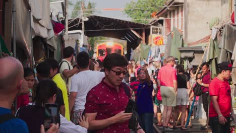 Toma-De-Establecimiento,-Un-Turista-Toma-Una-Fotografía-Y-Un-Video-Del-Tren-Que-Se-Aproxima-En-El-Mercado-De-Maeklong-En-Tailandia.