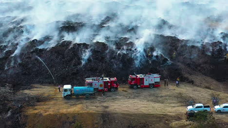 Aéreo,-Drone-Disparado-Sobre-Camiones-De-Bomberos-Y-Bomberos-Luchando-Contra-Un-Incendio-Forestal,-En-Un-Humo-Natural-Humeante-Que-Se-Eleva,-En-Un-Día-Nublado,-En-Santo-Domingo,-República-Dominicana