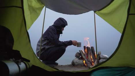 Statische-Aufnahme-Aus-Dem-Zelt-Eines-Wohnmobils,-Der-Sein-Warmes-Getränk-Trinkt-Und-Das-Lagerfeuer-Beobachtet