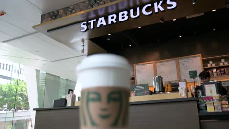 The-American-multinational-coffee-brand-Starbucks-Coffee-store-is-seen-in-the-background-as-a-coffee-paper-cup-stands-in-the-foreground