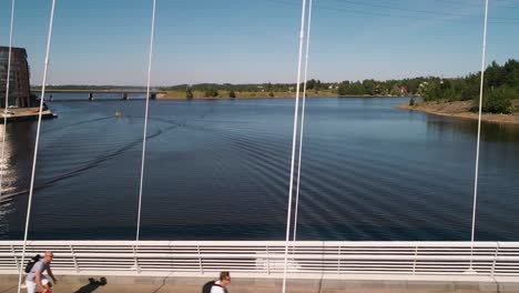 Aerial-view-overlooking-people-biking-on-a-white-bridge,-sunny-day,-in-the-Kalasatama-area,-Helsinki-city,-Uusimaa,-Finland---tracking,-drone-shot