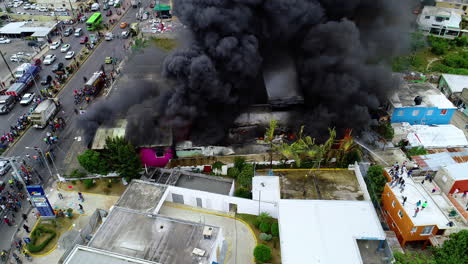 Aerial-view-of-a-burning-building,-a-dark-smoke-cloud-rising-from-the-raging-fire,-in-Santo-Domingo,-Dominican-Republic---Static,-drone-shot