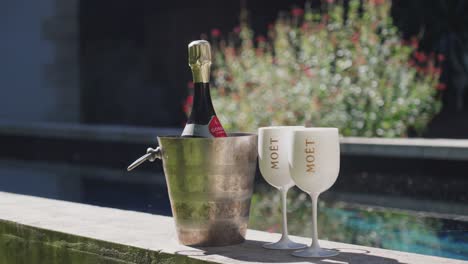 Botella-De-Champán-En-Una-Cubitera-Con-Hielo-Frío-Y-2-Vasos-De-Plástico-En-El-Exterior,-En-La-Pared-De-Terras