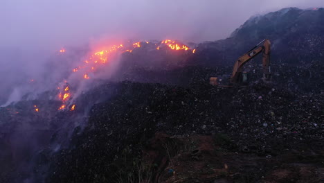 Aerial-view-of-a-digger-clearing-a-area-smoking-and-on-fire,-caused-by-a-bomb,,-war-and-terror-aftermath-in-the-Middle-east,-Asia---Pull-back,-drone-shot