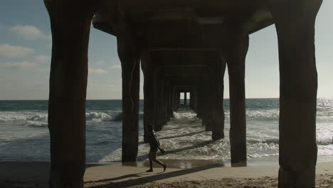 Toma-Cinematográfica-De-Un-Hombre-Caminando-Debajo-Del-Muelle-De-La-Playa-En-Cámara-Lenta-En-Cámara-Lenta