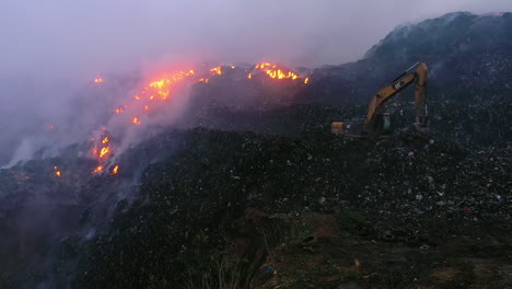 Aerial,-pull-back,-drone-shot-a-excavator-fighting-a-wildfire,-in-middle-of-flames-and-smoke,-on-a-dark-evening,-in-Los-Angeles,-California,-USA